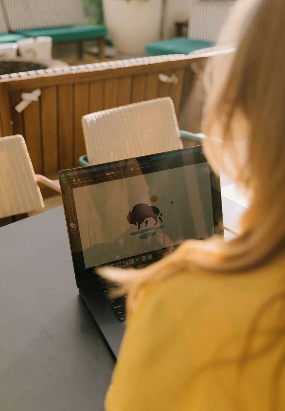 Over-the-shoulder view of a designer refining a logo on a laptop, showing ongoing brand stewardship and identity development for client brands.