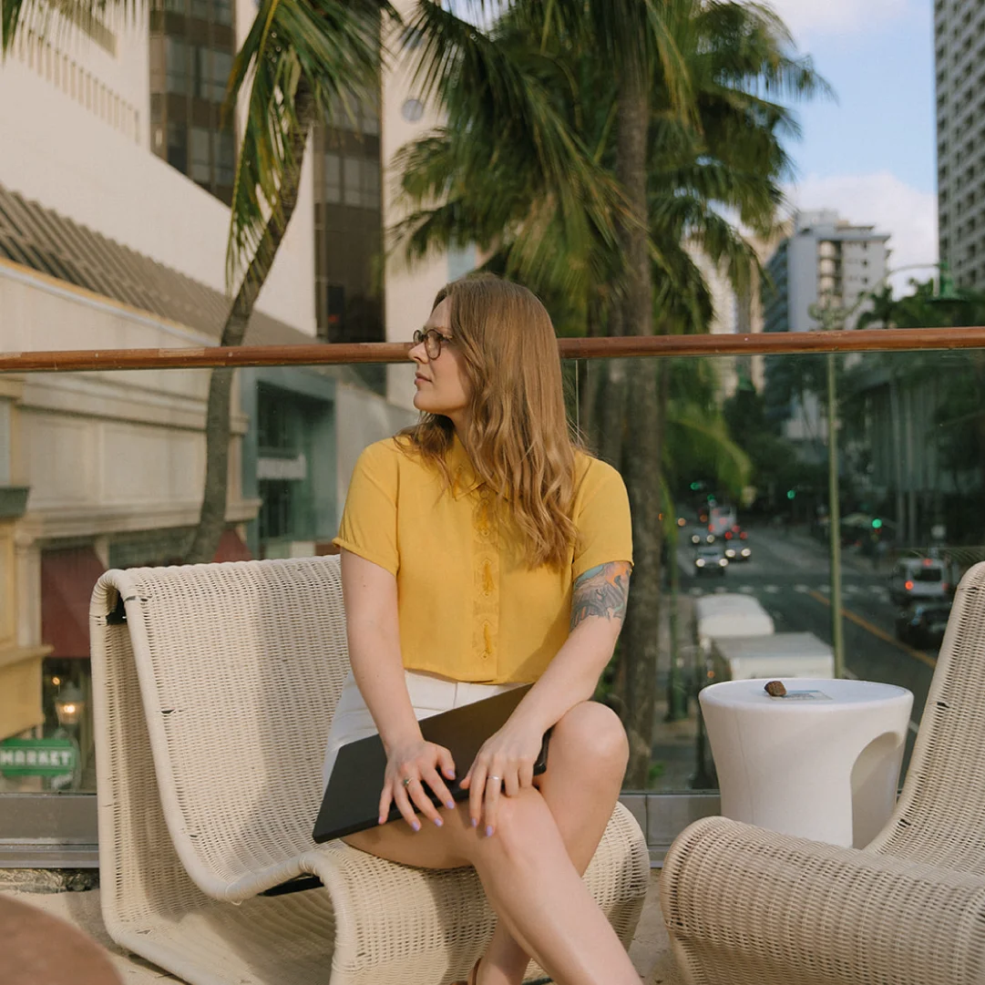 Creative director seated on a city hotel terrace with a laptop, representing remote strategy work for travel, tourism, and hospitality brands.