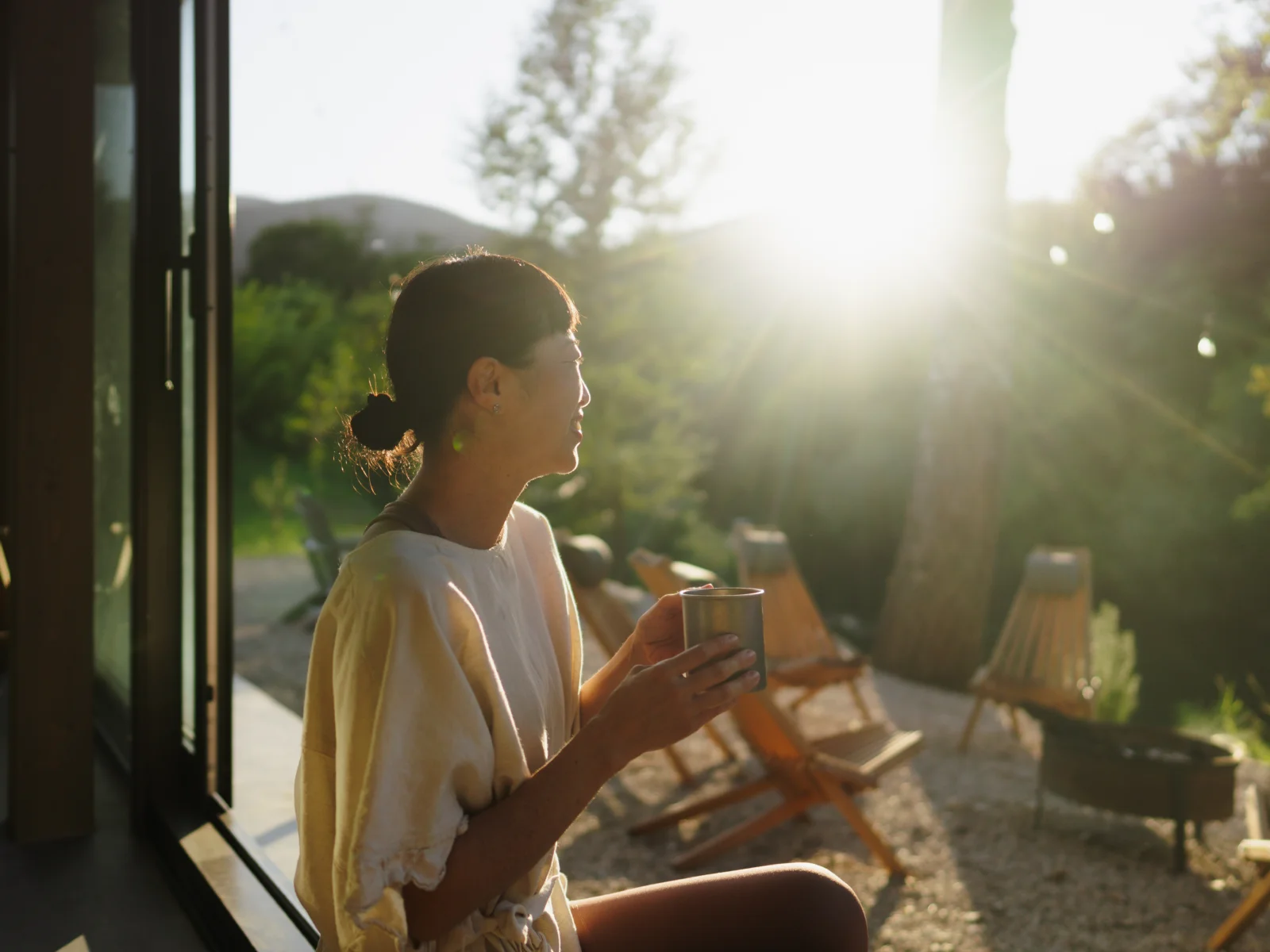 Guest holding a warm drink at sunset outside a nature retreat, capturing the calm and emotional experience that brings travellers back.