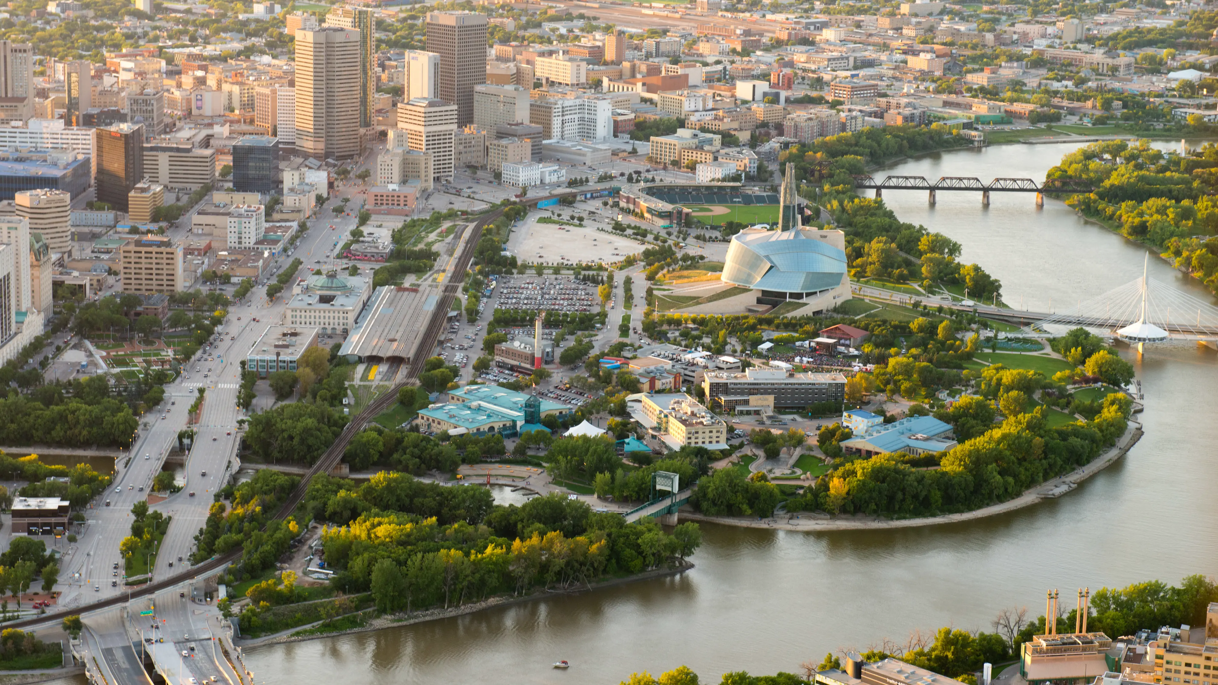 Aerial view of The Forks in downtown Winnipeg where the Red and Assiniboine Rivers meet, showing the site’s cultural landmarks and public gathering spaces.