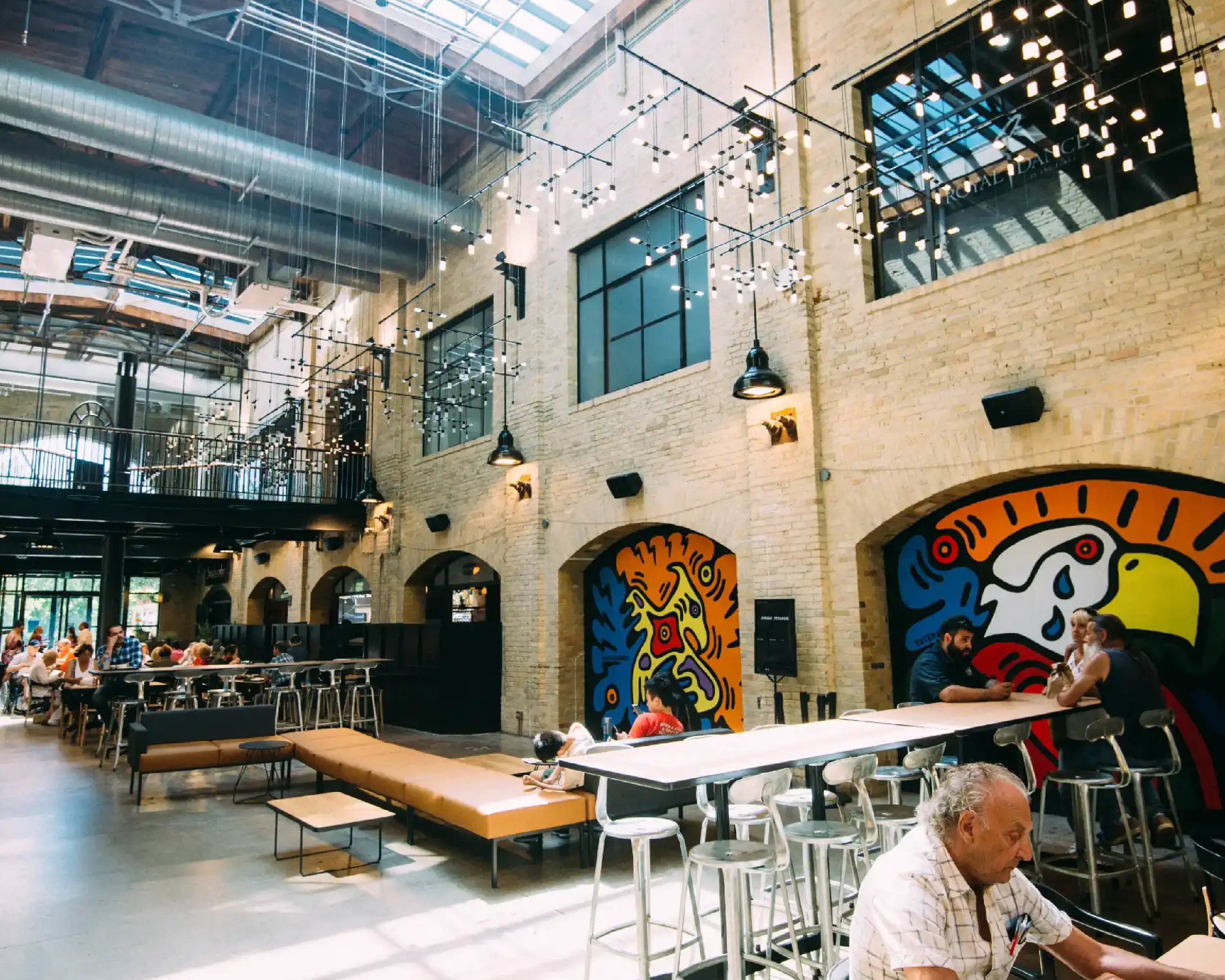 Interior of The Forks Market featuring exposed brick walls, murals, and café seating under string lights, a welcoming community gathering space.