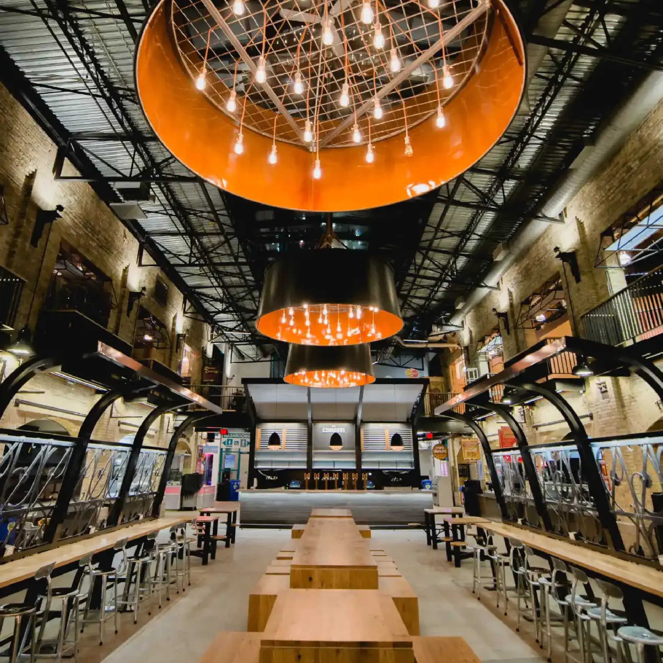 Interior of The Common bar at The Forks Market with modern orange lighting fixtures and communal wooden tables, a focal point of the venue.