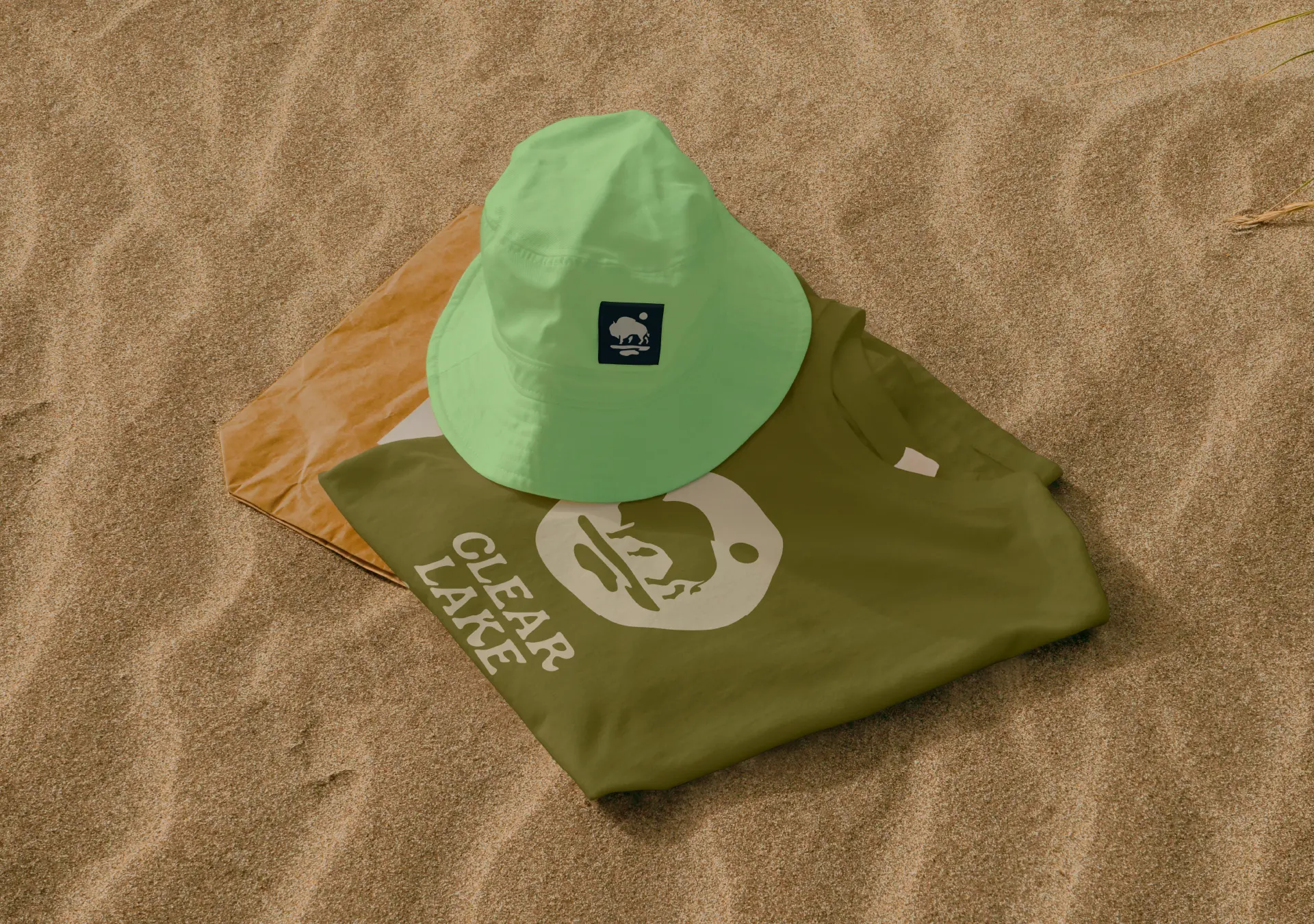 Clear Lake Country bucket hat and olive t-shirt with bison logo styled on beach sand in Riding Mountain National Park, Manitoba.