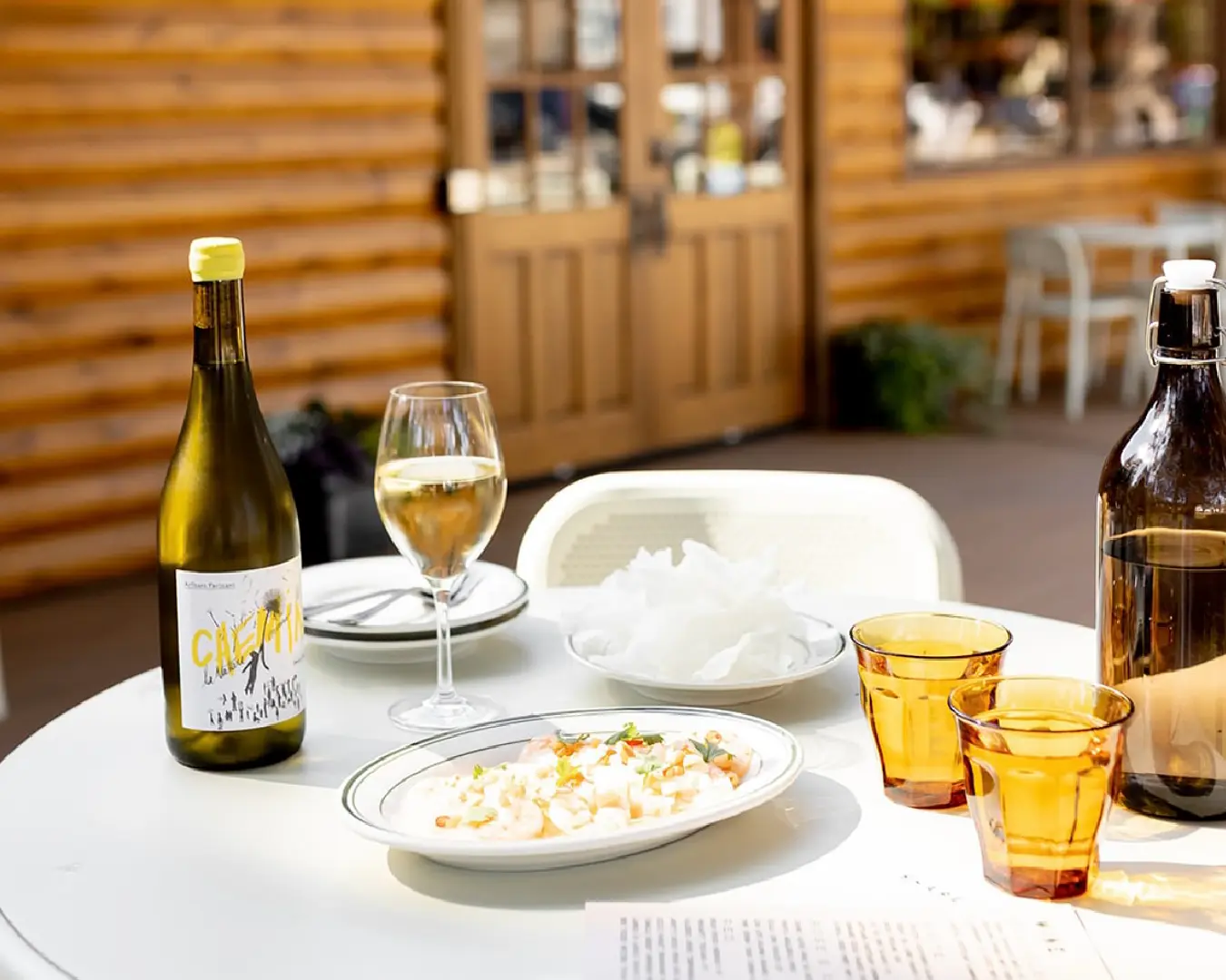 Outdoor table at Camp Cantina with a bottle of white wine, wine glass, amber tumblers, and shared snack plates.