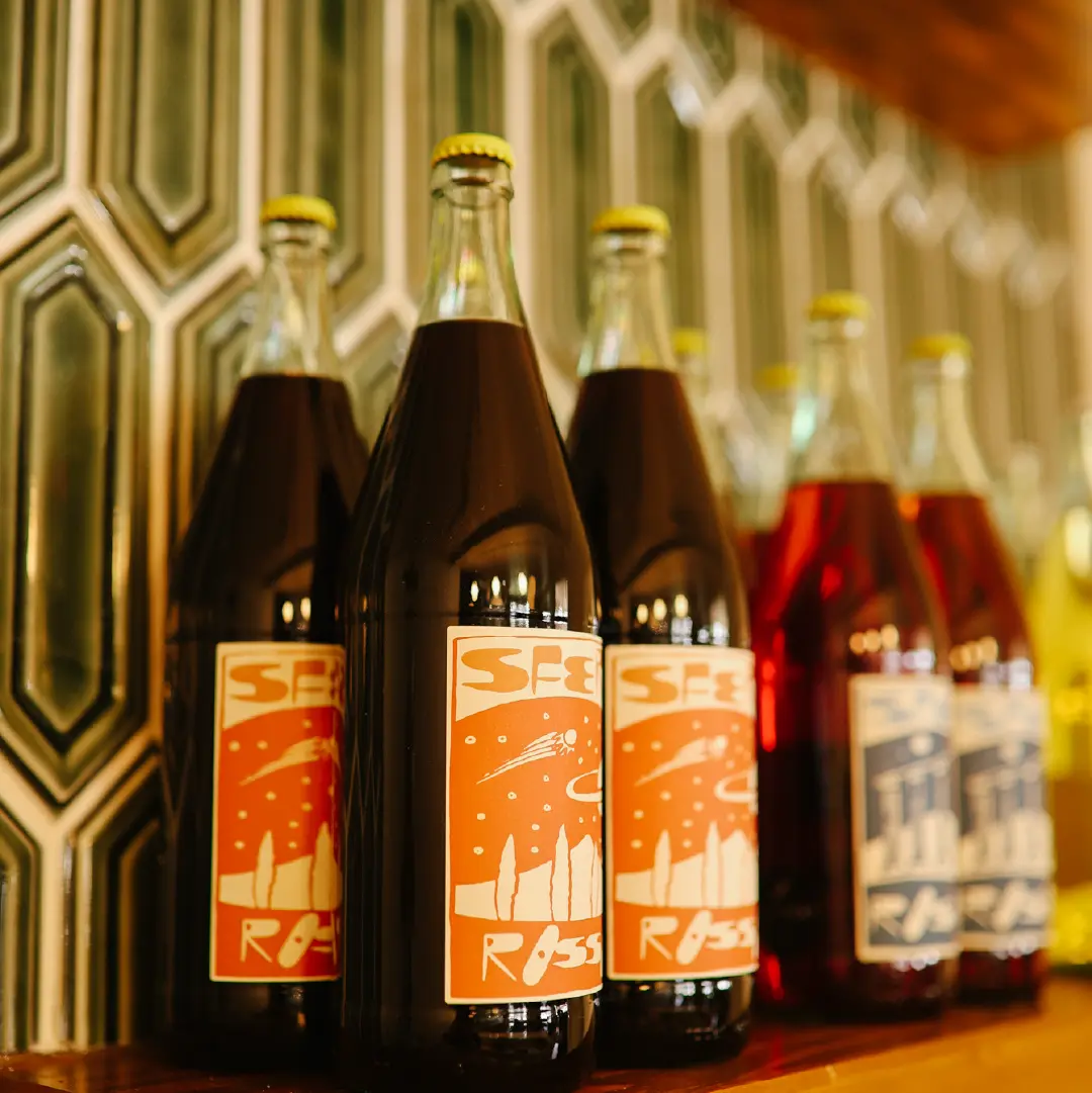 Bottles lined up on a shelf at Camp Cantina Wine Supply in Clear Lake, Manitoba, with colourful illustrated labels.