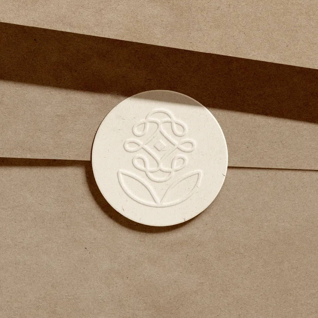 Embossed circular seal featuring the Reyou floral logo on textured paper with soft ribbon shadow lines.