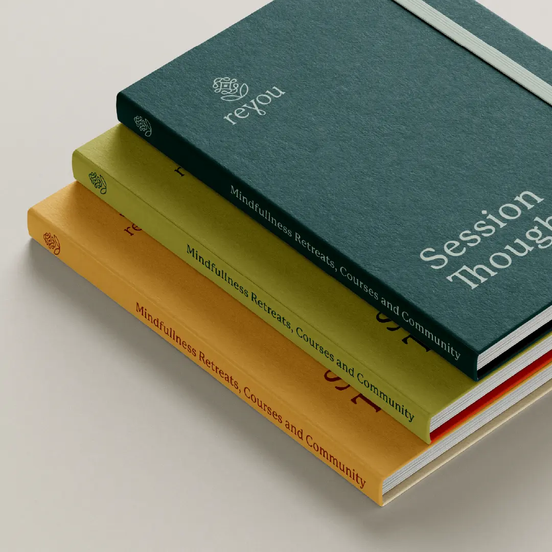 Stack of three Reyou journals in teal, green, and mustard with logo on covers and “Mindfulness Retreats, Courses and Community” on the spines.