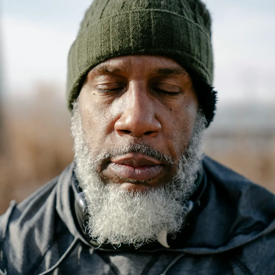 Close-up portrait of a man with eyes closed wearing a knit beanie, capturing a quiet moment of mindfulness and reflection outdoors.