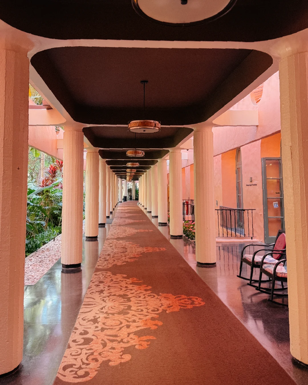 Long covered corridor at the Royal Hawaiian with pink walls, cream columns, and patterned flooring.
