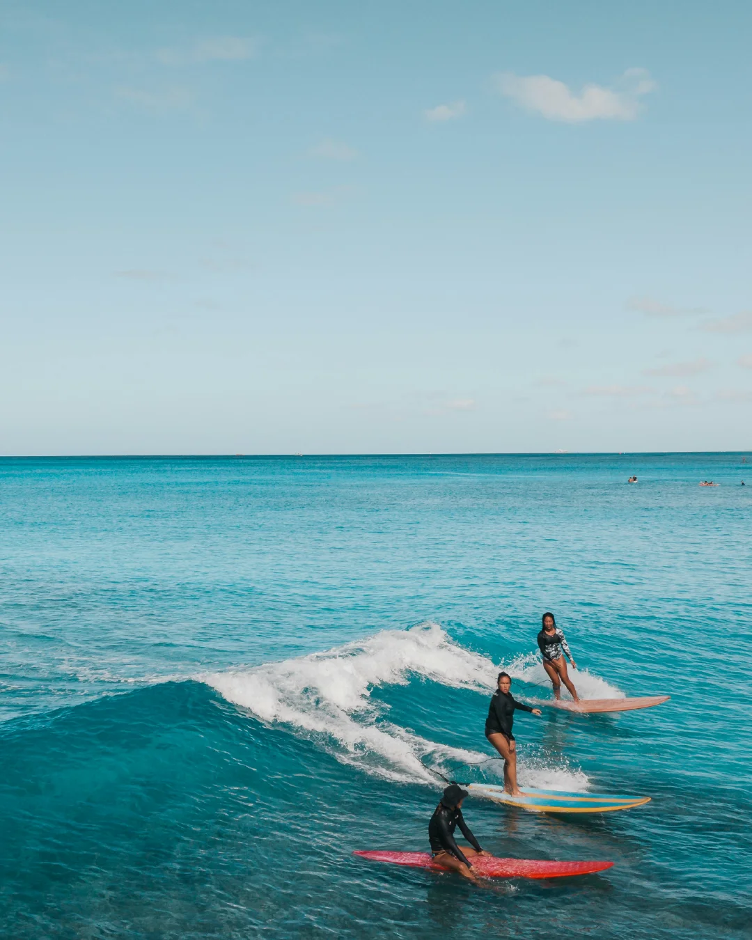 Surfers riding small waves in bright blue water off Waikiki Beach.