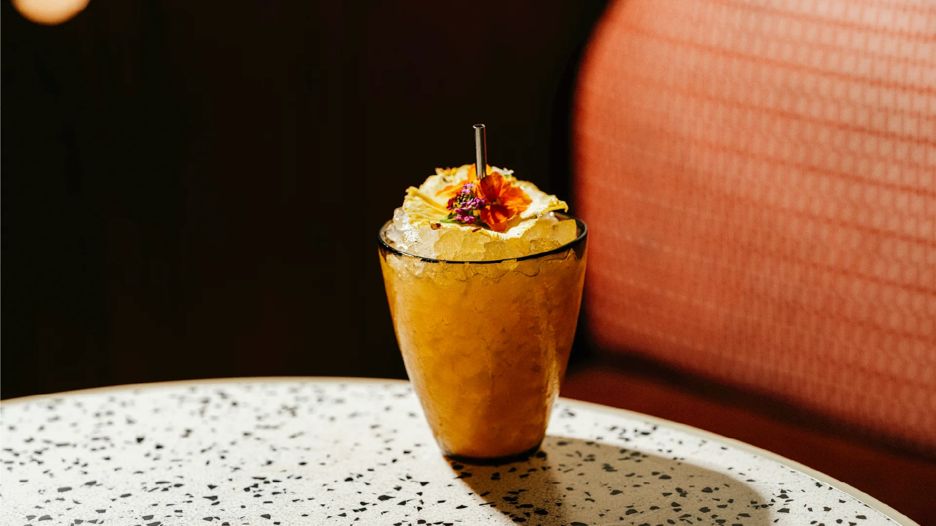 Tropical cocktail topped with flowers and dried pineapple on a speckled table inside the Royal Hawaiian.