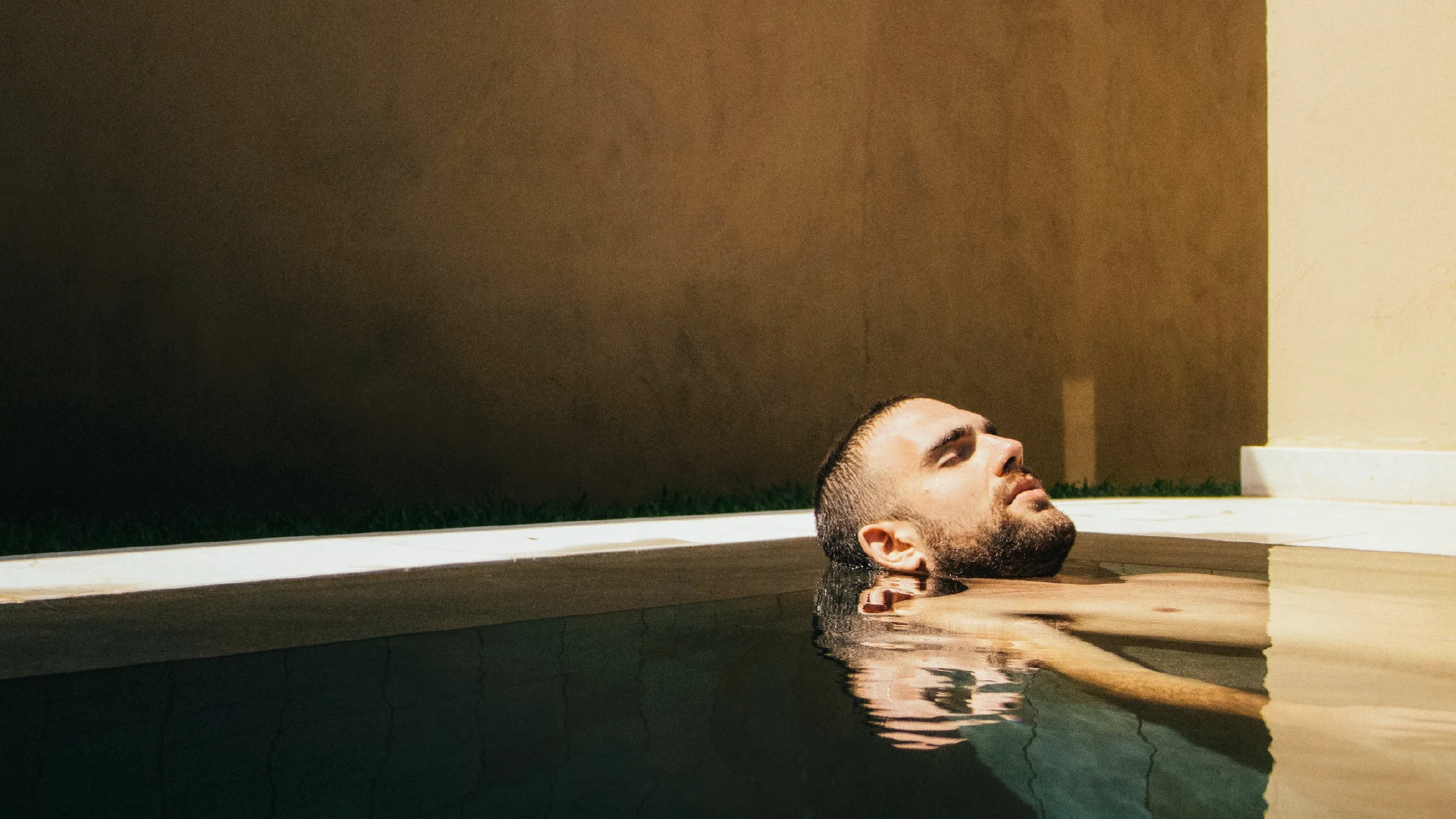 Guest resting in a dark indoor pool with warm light and minimal architectural surroundings.