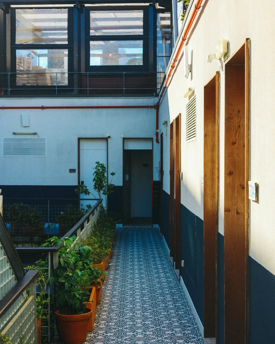 Interior corridor with patterned tile floors, potted plants, wood-trimmed doors, and an open-air courtyard feel.