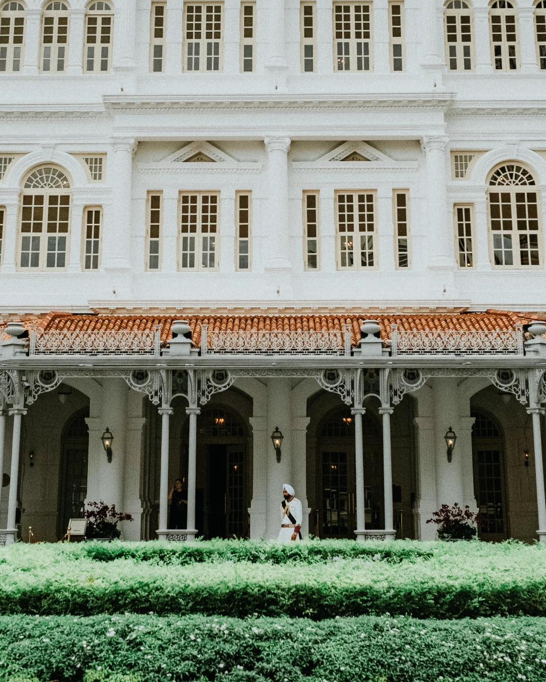 Grand historic white hotel exterior with arched windows, columns, and a guard standing in the courtyard.