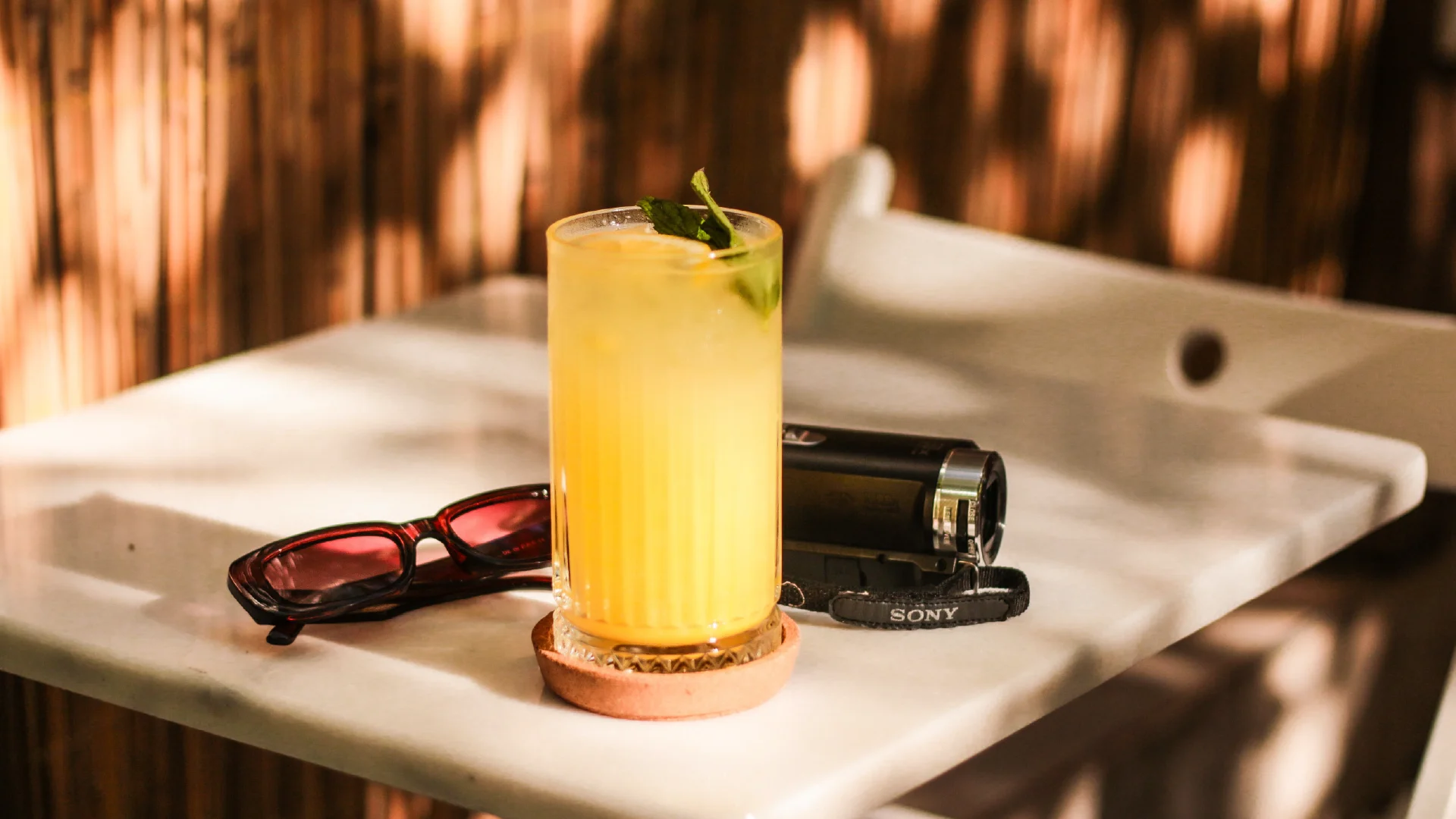A bright welcome drink beside sunglasses and a camera, capturing a warm hospitality experience.