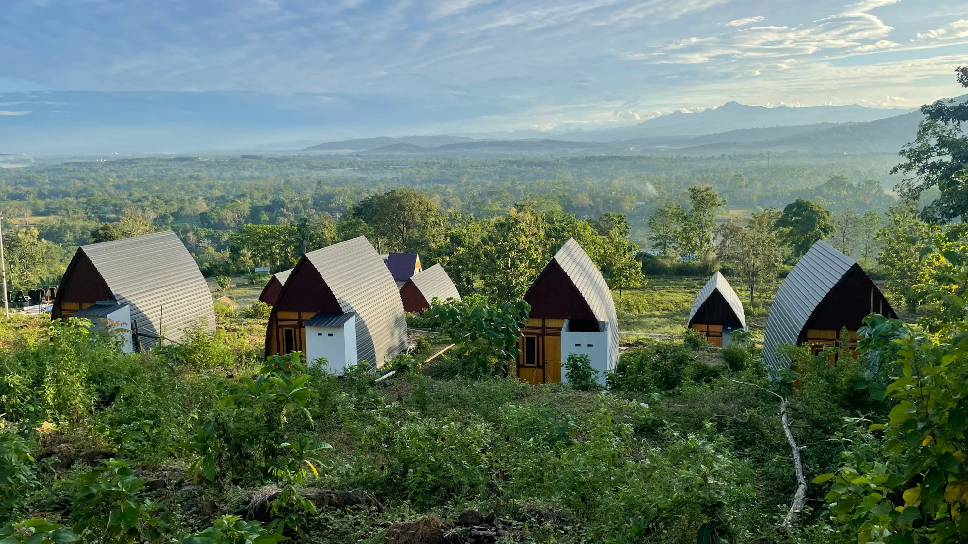 Small cabin stays on a green hillside overlooking a misty valley and mountain landscape.