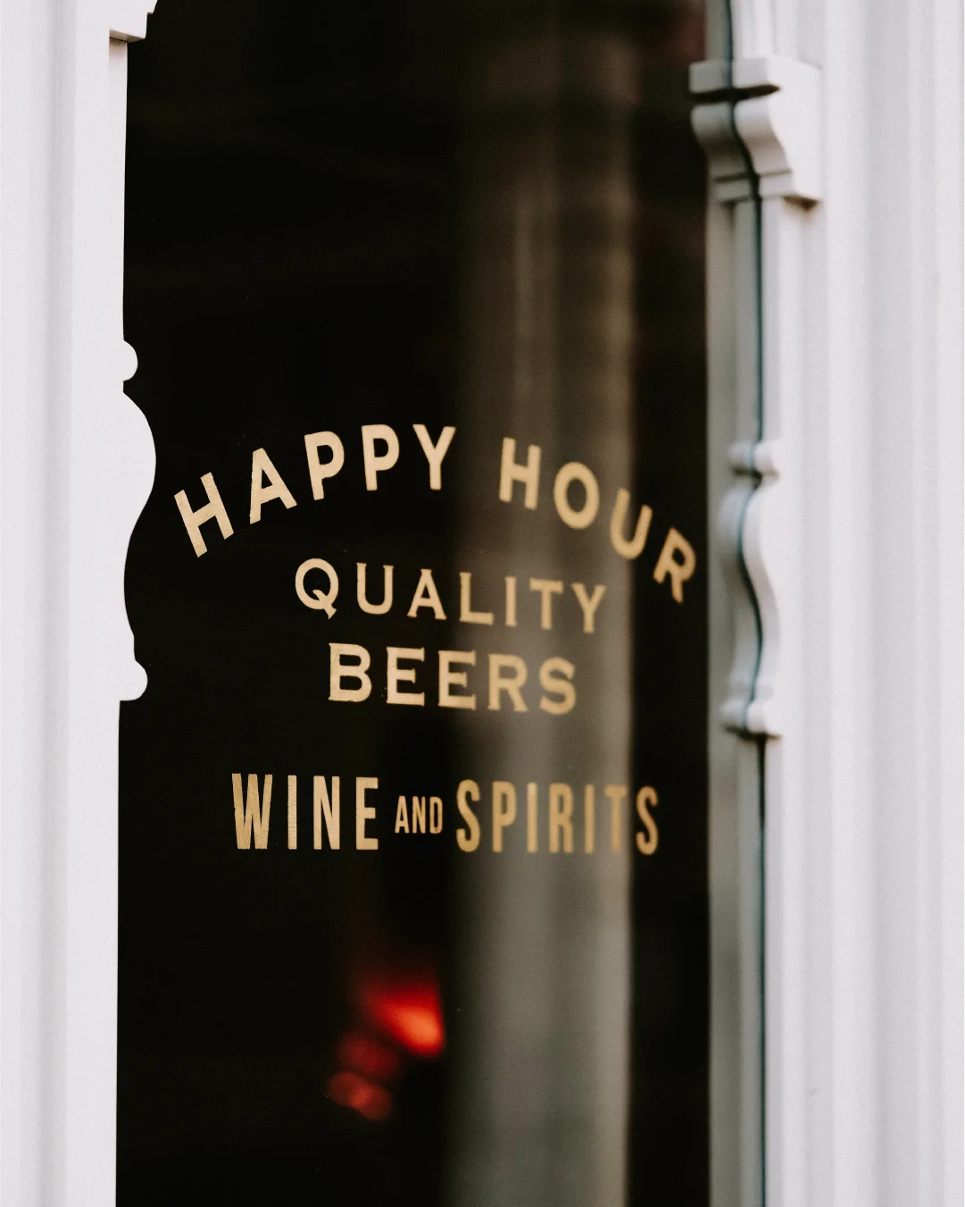 Close-up of a restaurant window with gold lettering that reads “Happy Hour,” “Quality Beers,” and “Wine and Spirits.”
