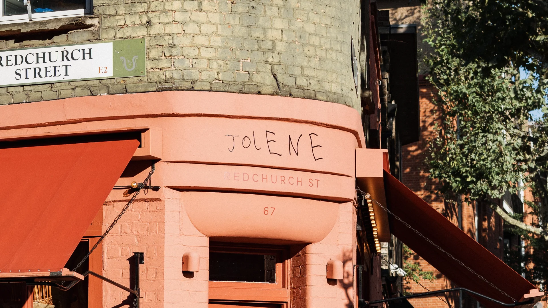 Close-up of the peach-painted Jolene restaurant exterior on Redchurch Street with awnings, brickwork, signage, and warm sunlight.