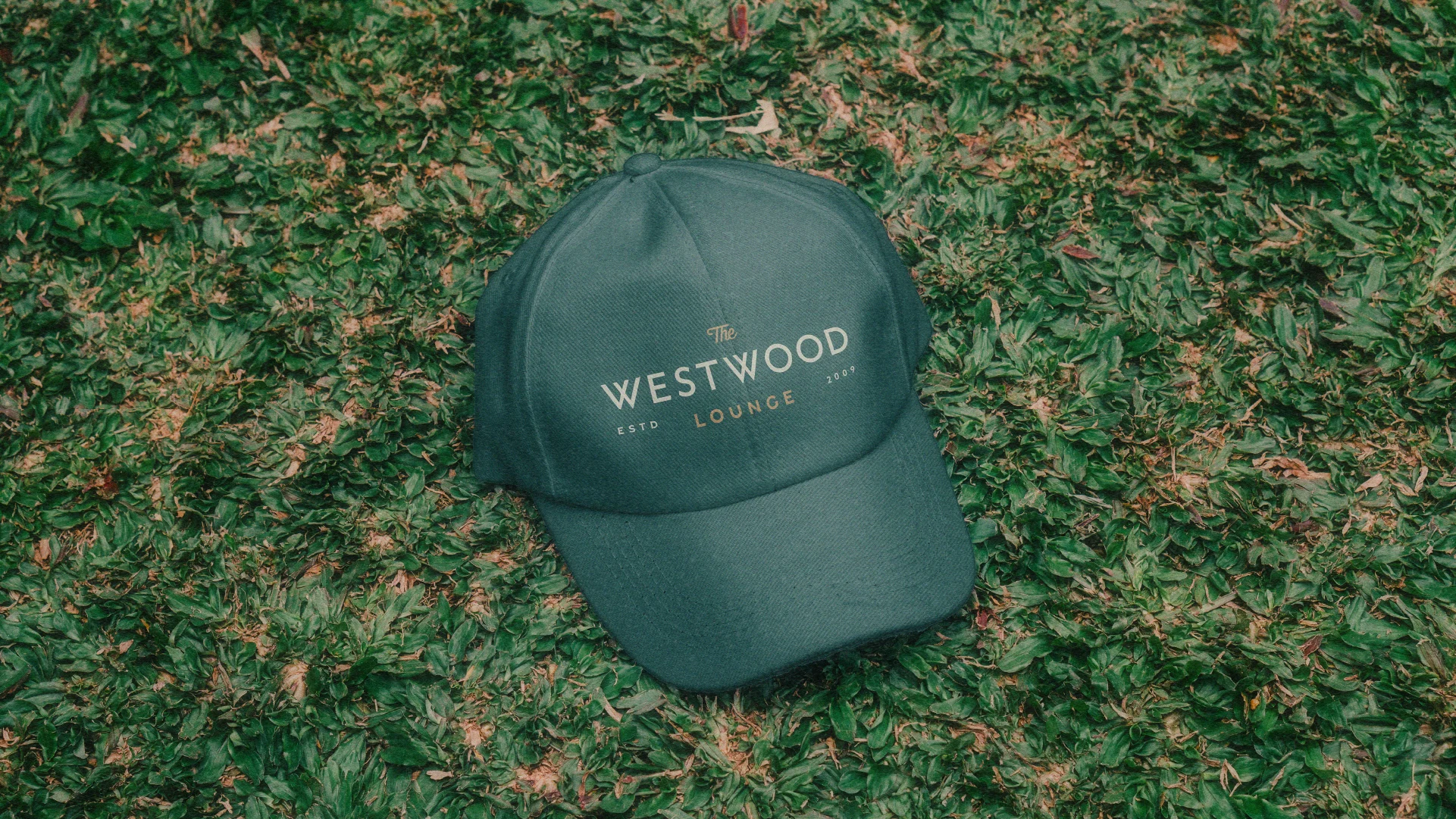 Green Westwood Lounge branded hat displayed on grass as part of the restaurant and pub merchandise system.