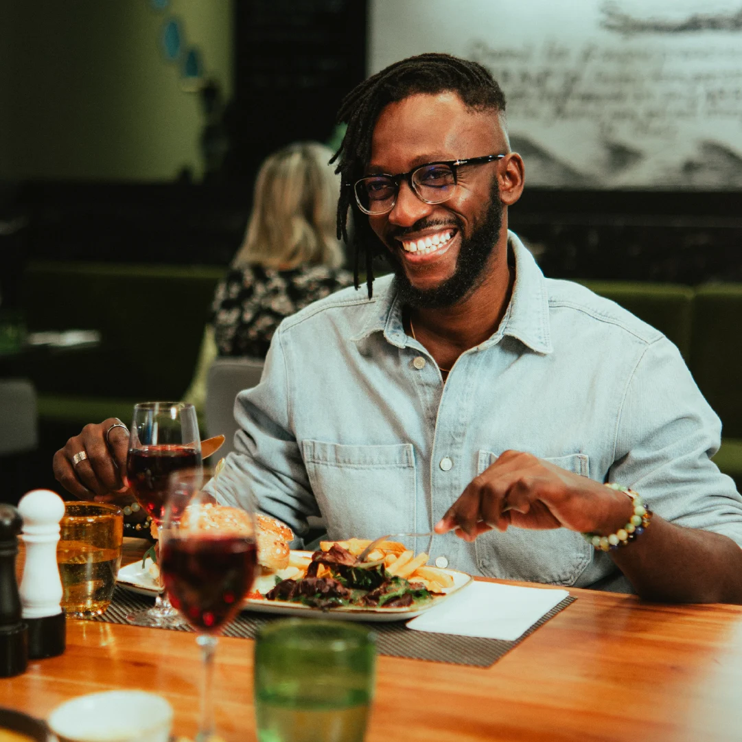 Guest smiling while dining at Westwood Lounge with food and drinks in the restaurant interior.