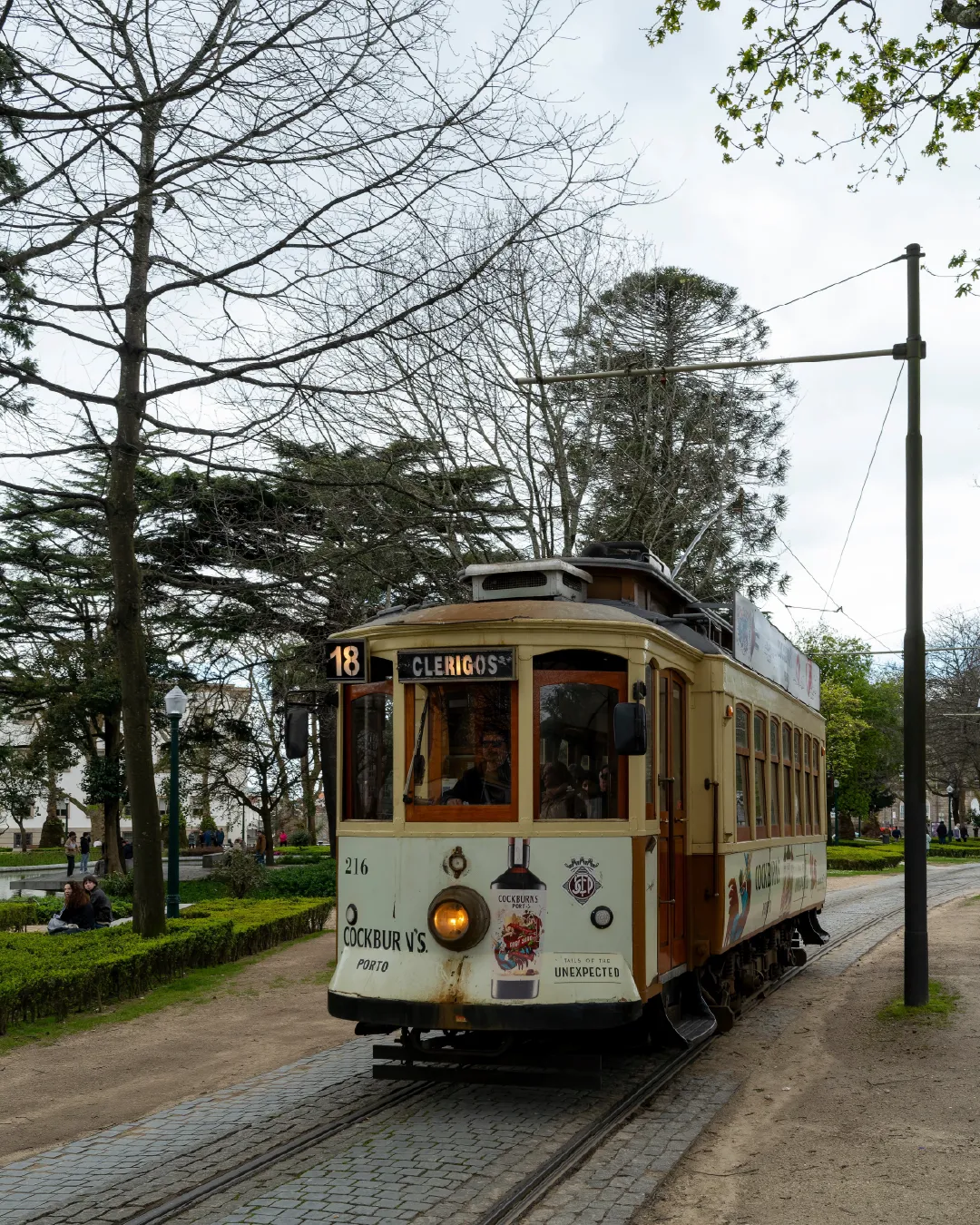 Vintage yellow tram travelling along tracks through a leafy park in Porto, Portugal, surrounded by trees and historic streetscape details.
