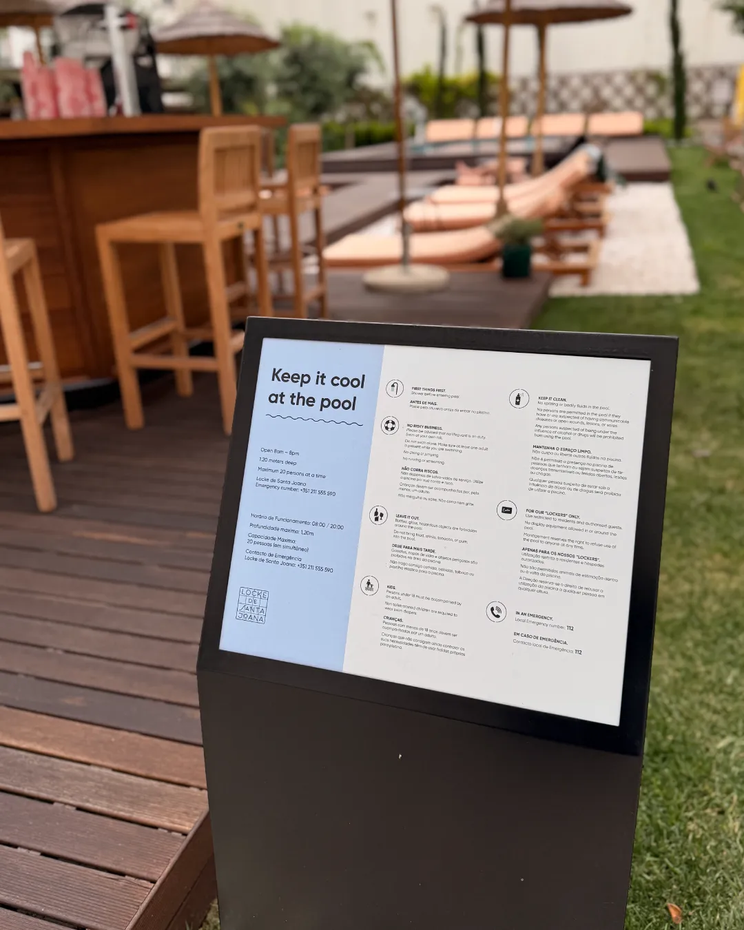 Pool rules sign with branded typography beside an outdoor hotel pool deck with lounge chairs and umbrellas.