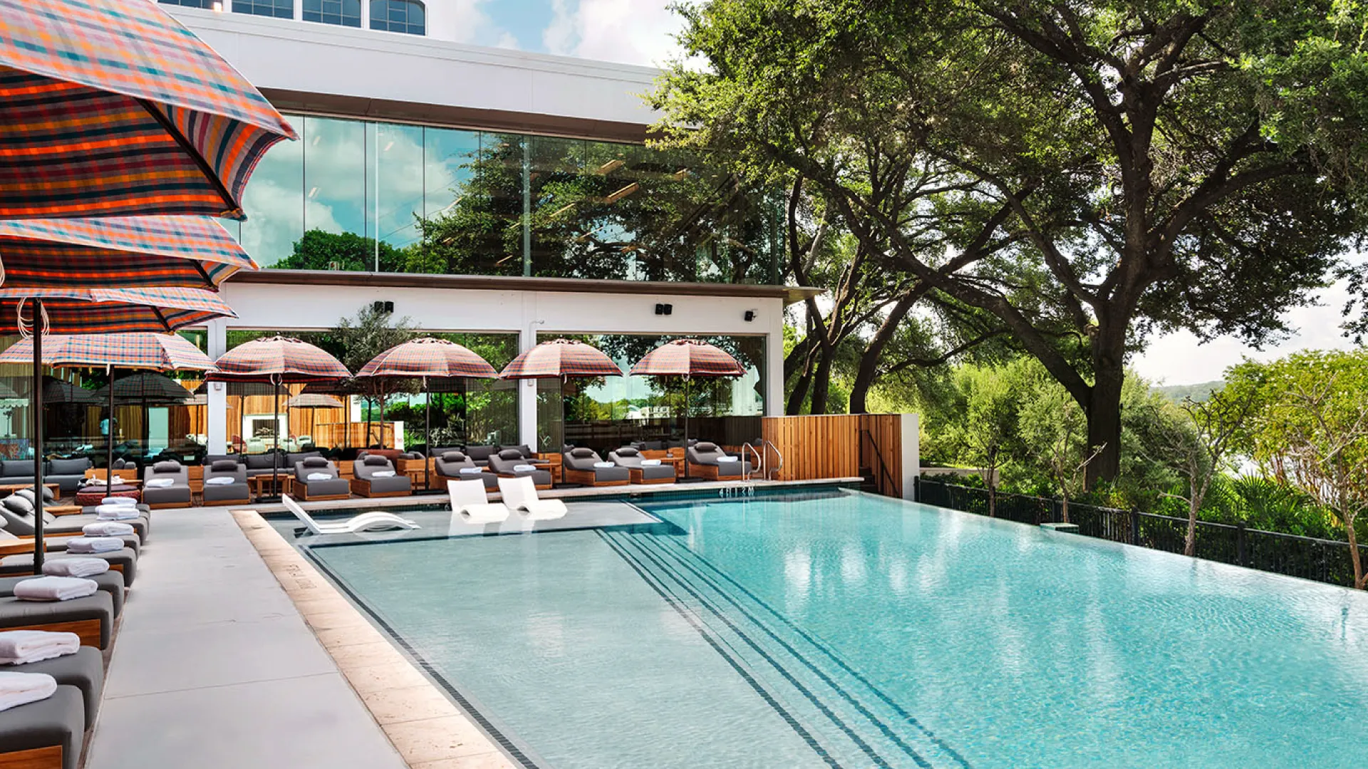 Outdoor pool at The LINE Austin with lounge chairs, patterned umbrellas, trees, and modern hotel architecture.