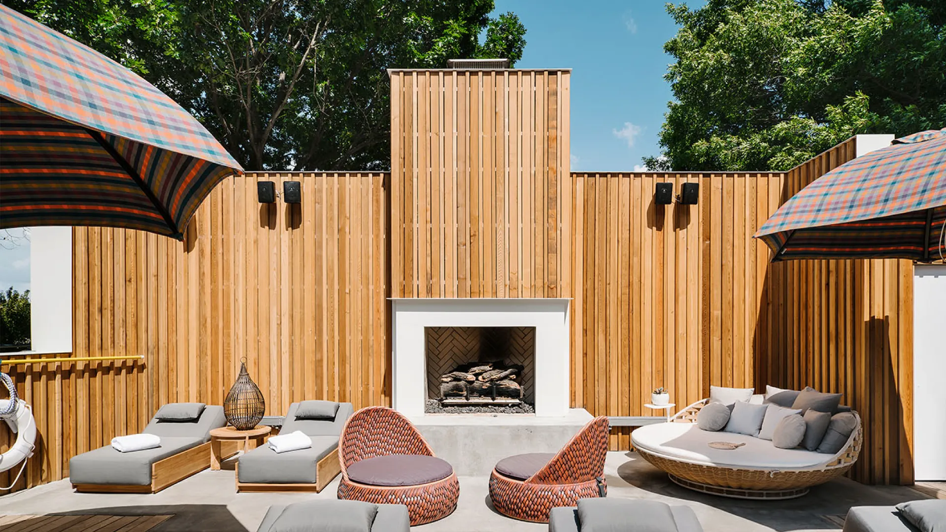 Poolside lounge area at The LINE Austin with woven chairs, daybeds, wood fencing, and a central outdoor fireplace.