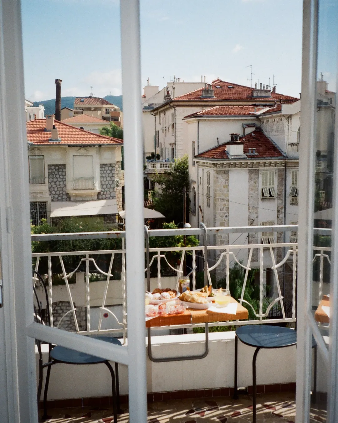 Breakfast set on a small hotel balcony overlooking red-tiled rooftops and residential buildings.