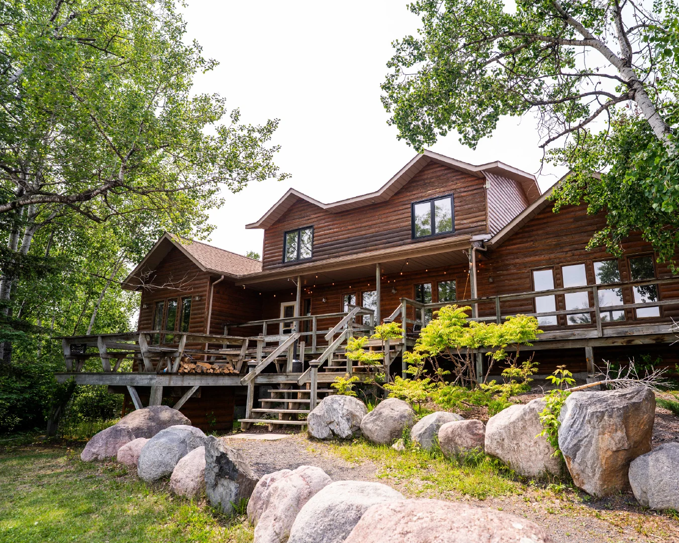 Exterior of The Lodge at Perch Bay, a rustic log wedding and events venue surrounded by trees and granite boulders.