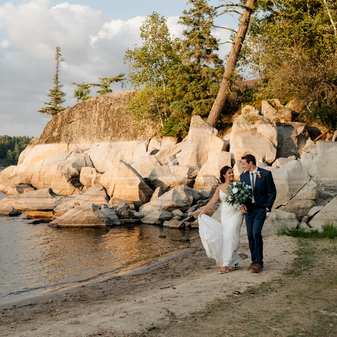 Newly married couple walking along the rocky waterfront at The Lodge at Perch Bay wedding venue in Northern Ontario.