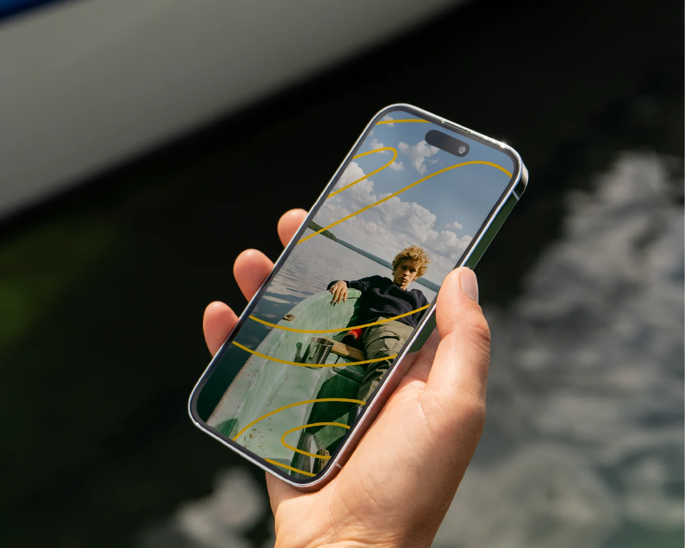 Hand holding a smartphone displaying a young person relaxing in a boat, accented with yellow Perch Bay brand graphics.
