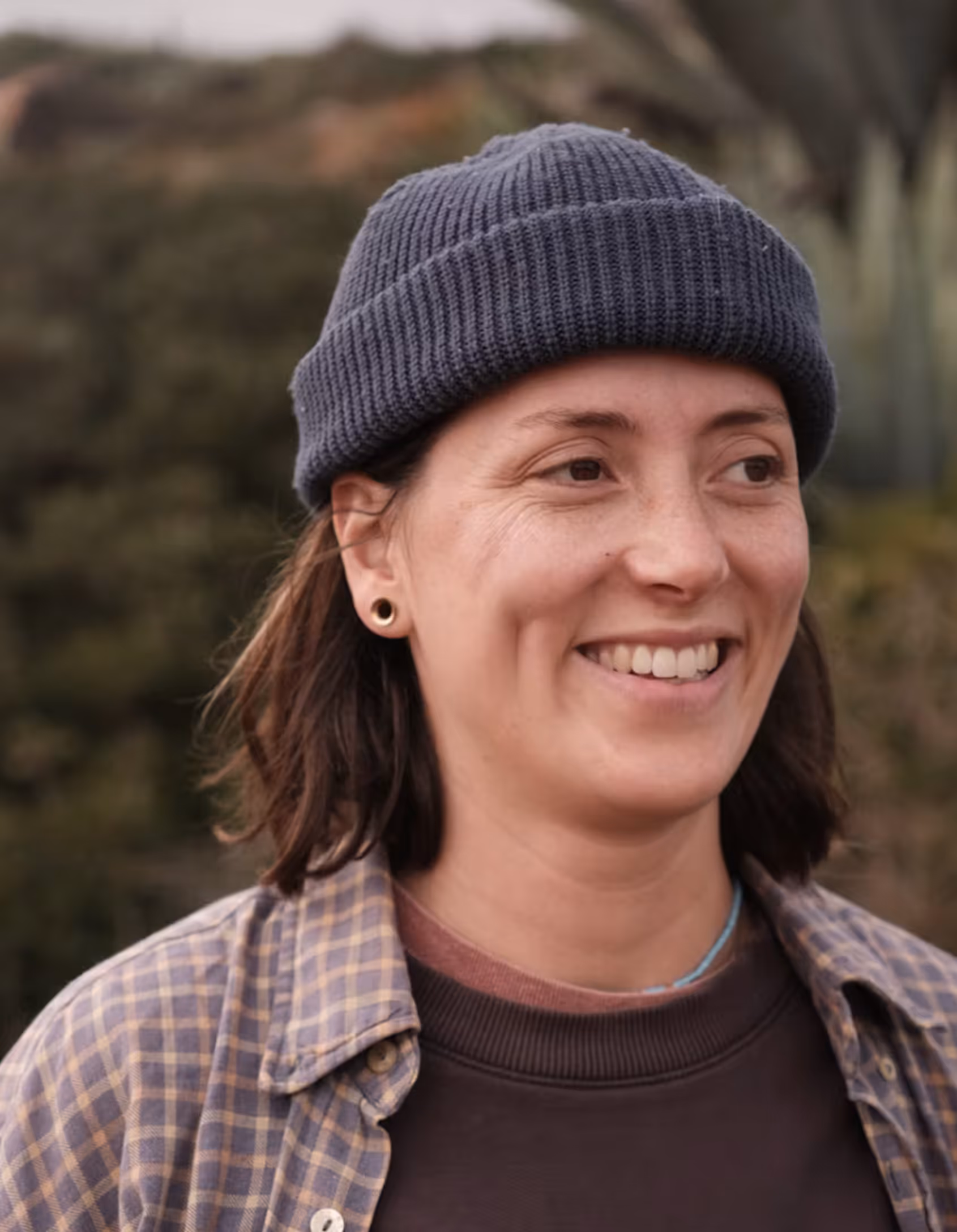 Close up of a young woman's face, she's standing outside, wearing a beanie and smiling