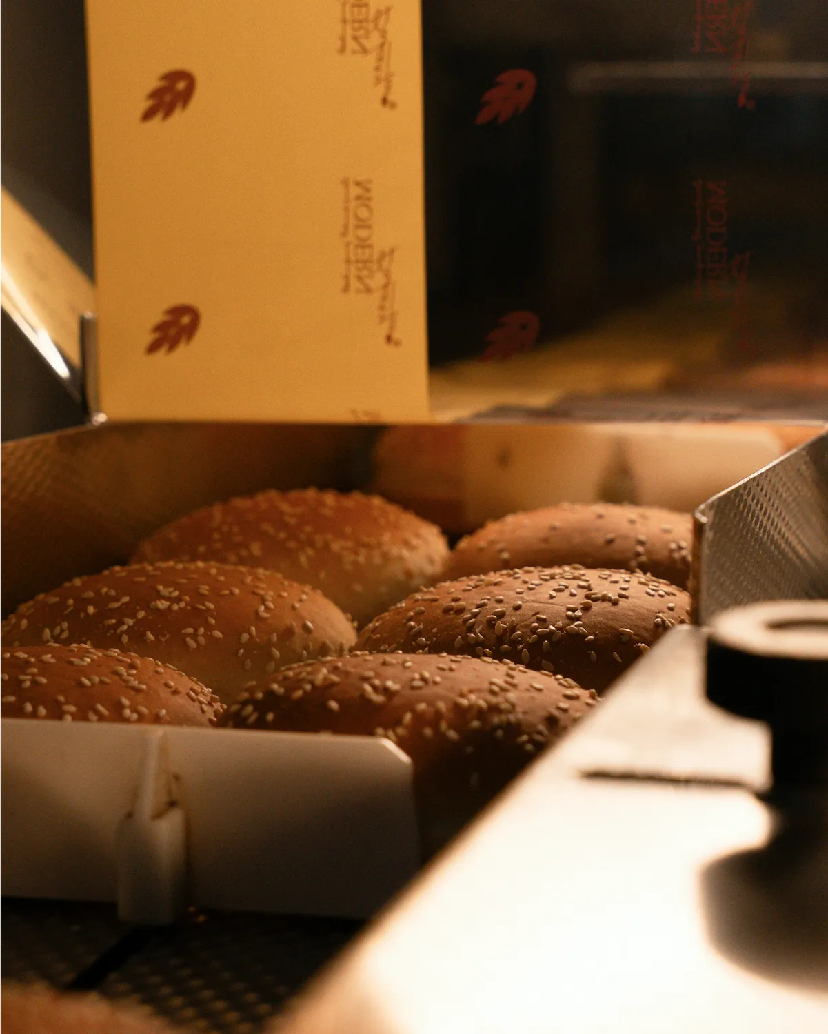Sesame seed burger buns arranged in a tray inside a bakery oven.
