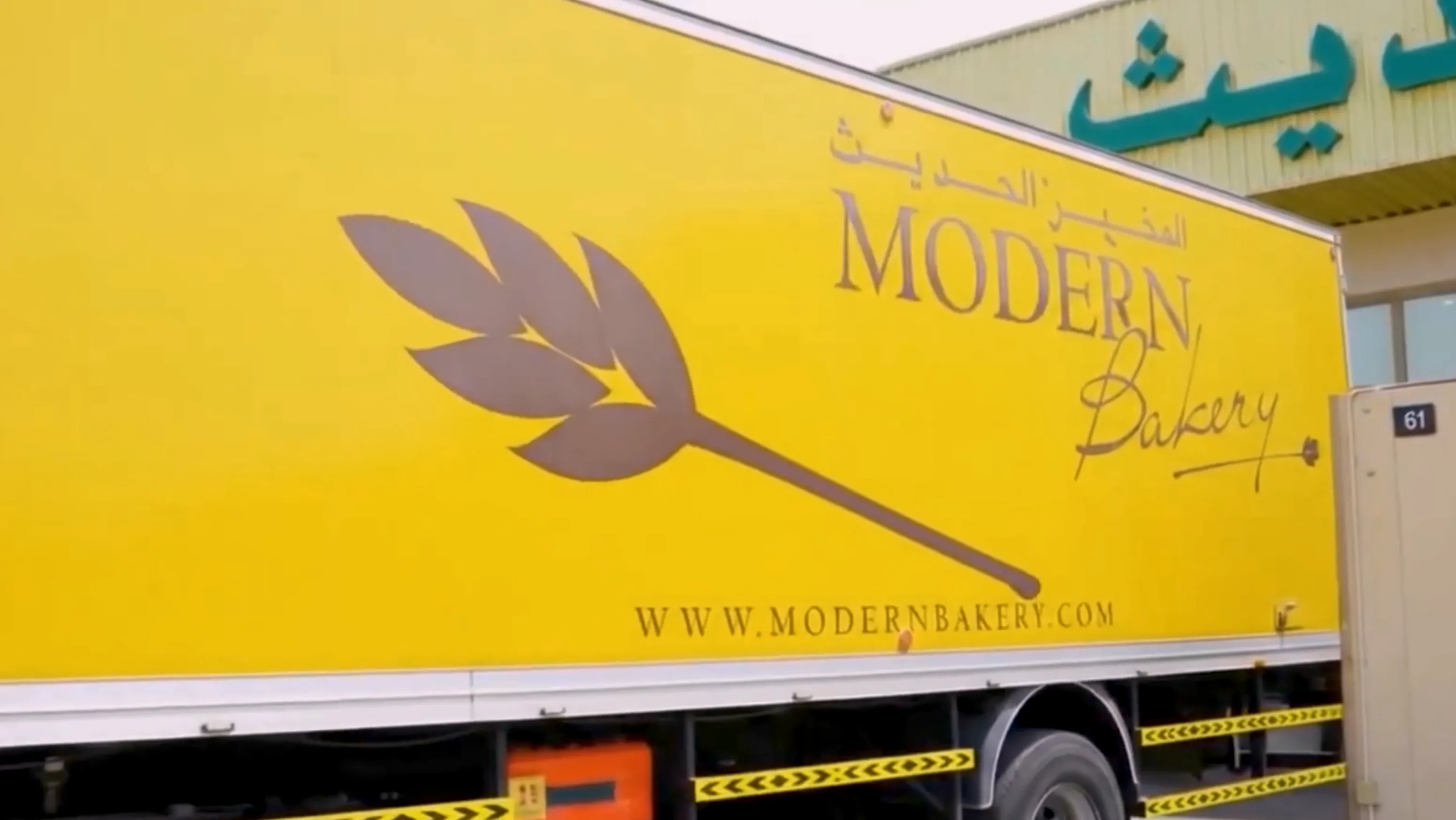 Yellow delivery truck with Modern Bakery logo, including a stylized wheat graphic and website URL.