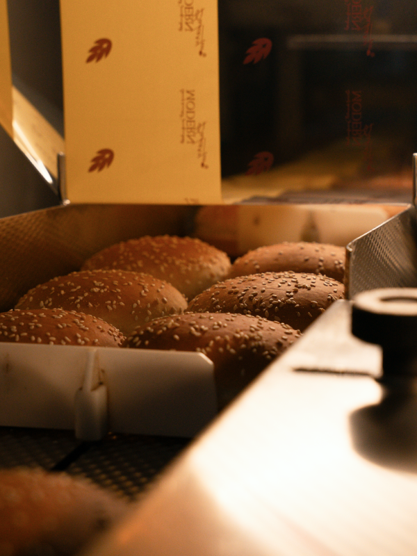 Sesame seed hamburger buns on a conveyor belt inside a bakery oven.