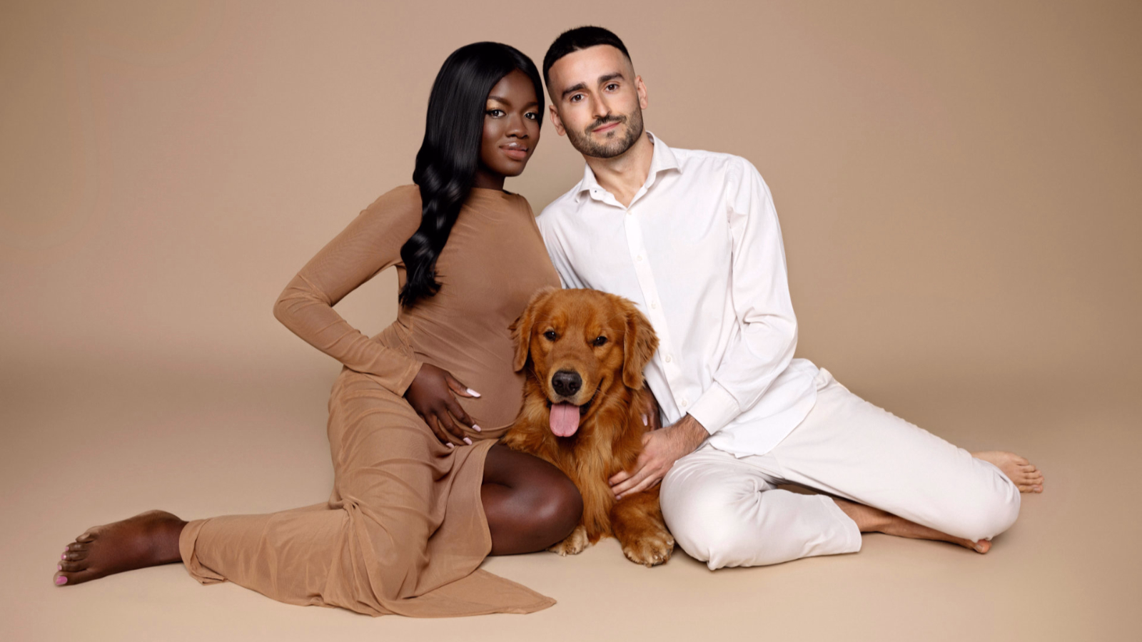 Foto di coppia in attesa con golden retriever, donna incinta in abito marrone e uomo in bianco, ritratto di famiglia in studio fotografico a Bologna.