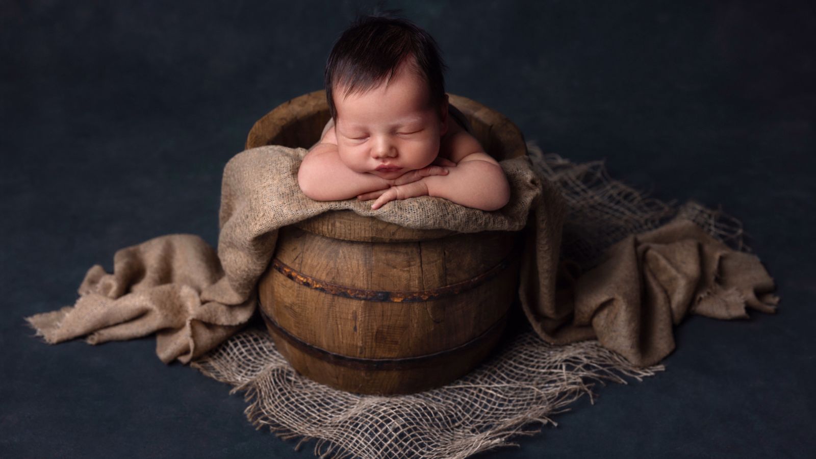 Ritratto newborn di neonato che dorme in una botte di legno con tessuto rustico, fotografia artistica realizzata da Claudia Spaziani nel suo studio fotografico a Bologna.