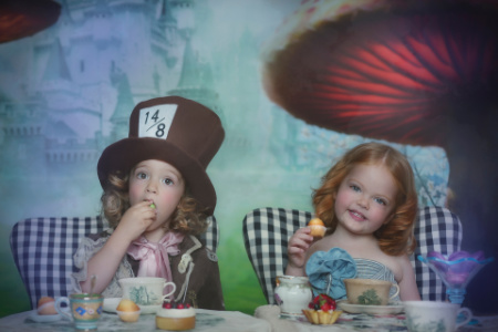 Bambini in costumi di Alice e Cappellaio Matto a tavola con tè e dolci in servizio fotografico fiabesco.