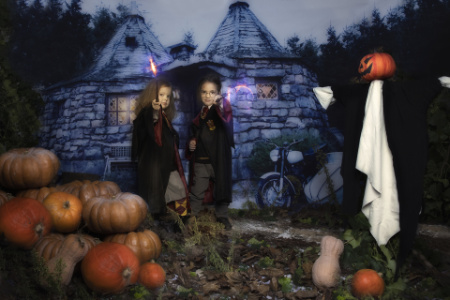 Bambini in costume da mago con bacchette luminose davanti a cottage in pietra e zucche in servizio fotografico fantasy ispirato a Harry Potter.