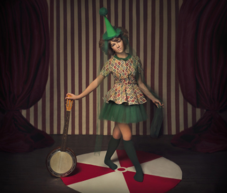 Modella in costume da circo su pedana rossa e bianca in servizio fotografico artistico fiabesco.