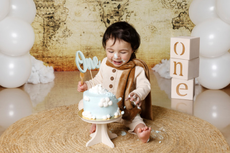 Bambino con torta a tema nuvole e mappa vintage in servizio fotografico smash cake primo compleanno.
