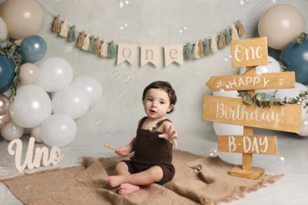 Bambino circondato da palloncini colorati in set fotografico smash cake per primo compleanno.