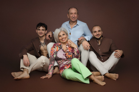 Foto di famiglia multigenerazionale in studio fotografico a Bologna – Claudia Spaziani – Quattro persone sedute, coppia matura e due giovani, abbigliamento casual elegante, sfondo marrone neutro.