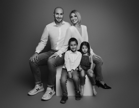 Ritratto di famiglia in bianco e nero con due bambini a Bologna – Claudia Spaziani – Coppia seduta con figlio e figlia davanti, abbigliamento casual coordinato, sfondo scuro.