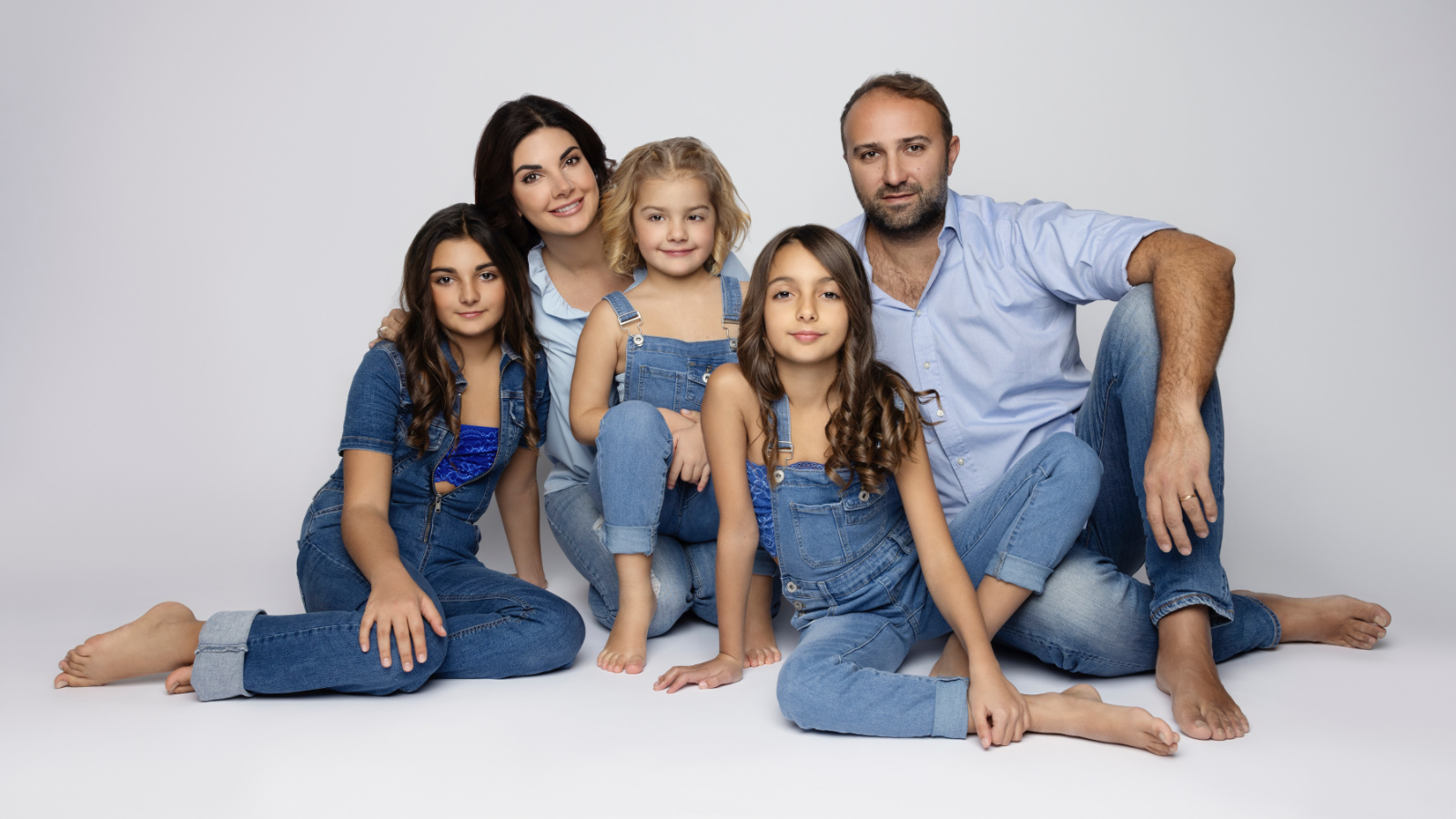Servizio fotografico di famiglia in denim a Bologna – Claudia Spaziani – Due adulti e tre bambine in jeans e salopette, posa ravvicinata su sfondo bianco, look casual e armonioso.
