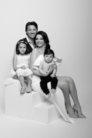 Foto di famiglia in bianco e nero con posa moderna a Bologna – Fotografa Claudia Spaziani – Coppia con due figli su blocchi bianchi geometrici, abiti eleganti, sfondo chiaro minimalista.