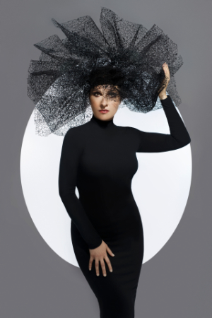 Ritratto fine art di Luisa, artista, in abito a collo alto nero con maxi copricapo in tulle nero a raggiera, posata davanti a un cerchio di luce bianca su sfondo grigio — look scenografico e teatrale; book fotografico per artisti di Claudia Spaziani, Castel Guelfo di Bologna