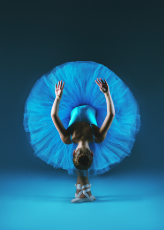 Ritratto artistico di ballerina classica fotografata di spalle: tutù azzurro cielo aperto a cerchio perfetto, body turchese, scarpette da punta bianche e braccia sollevate in arabesque su sfondo sfumato blu profondo — book fotografico per danzatori e performer di Claudia Spaziani, Bologna