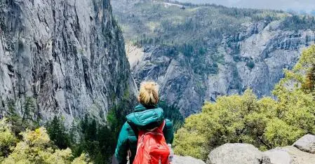 one woman in the mountains with a red backpack from behind